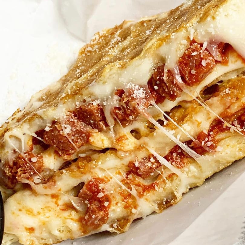 Close-up of a calzone slice filled with melted cheese, pepperoni, and sprinkled with parmesan.