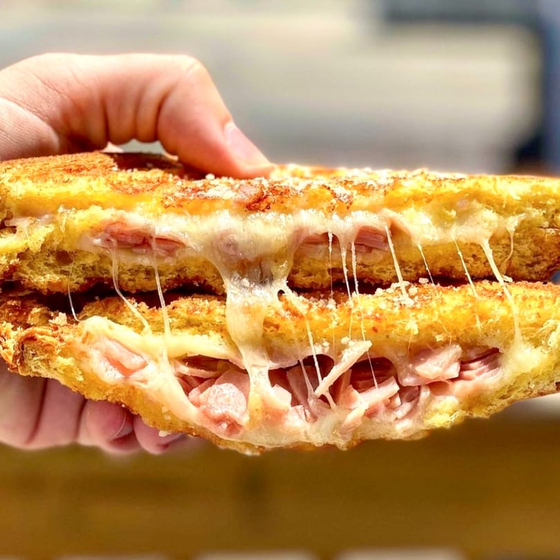Hand holding a grilled cheese sandwich with melted cheese and ham stretching between the halves.