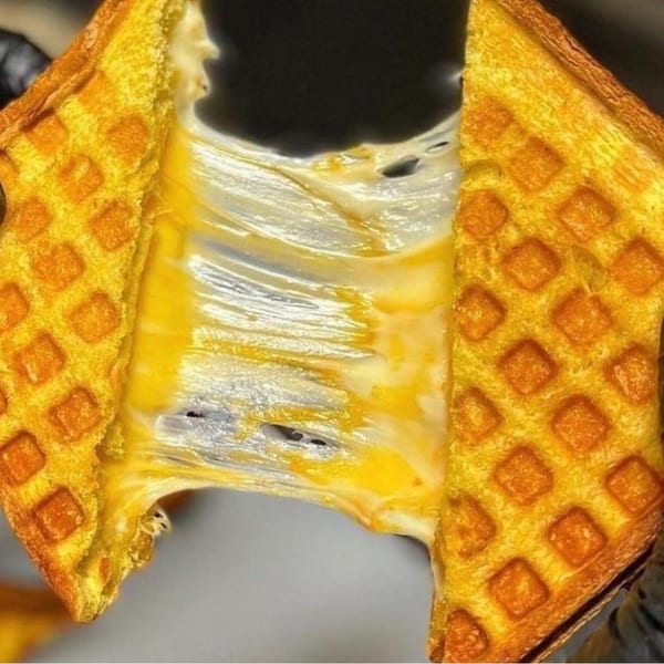A waffle-pressed grilled cheese sandwich pulled apart, revealing gooey, melted cheese stretching between the halves.